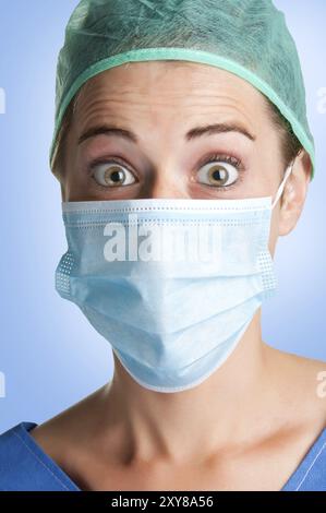 Closeup portrait of a surpris chirurgienne, avec un masque, dans un fond bleu Banque D'Images