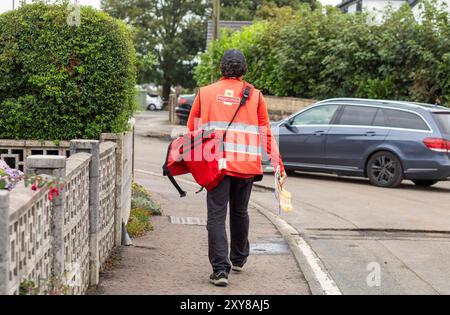 Un facteur effectue des livraisons dans le village de Northowram, dans le West Yorkshire, à Calderdale, au Royaume-Uni. Royal mail Group Limited, opérant sous le nom de Royal mail, est une société britannique de services postaux et de messagerie. Elle appartient à International distribution services. Elle exploite les marques Royal mail (lettres et colis) et Parcelforce Worldwide (colis). Crédit : Windmill images/Alamy Live News Banque D'Images