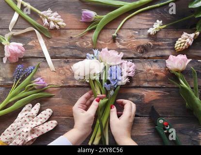 Un fleuriste au travail. Femme faisant bouquet de fleurs de printemps sur la table en bois rustique Banque D'Images