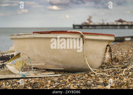 Un bateau cassé sur la plage de galets de Herne Bay, Kent, Angleterre, Royaume-Uni, avec Herne Pier en arrière-plan Banque D'Images