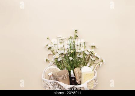 Concept d'été écologique sur fond beige avec sac d'achats écologique, fleurs de camomille blanches, accessoires de bain, brosses, bouteille d'huile essentielle, savon Banque D'Images