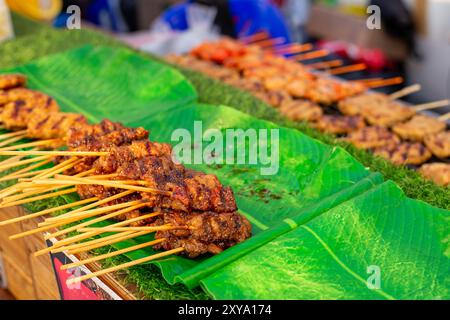 Nourriture de rue. Brochettes de viande cuites sur feuille de banane à un étal de marché nocturne en Asie. Banque D'Images