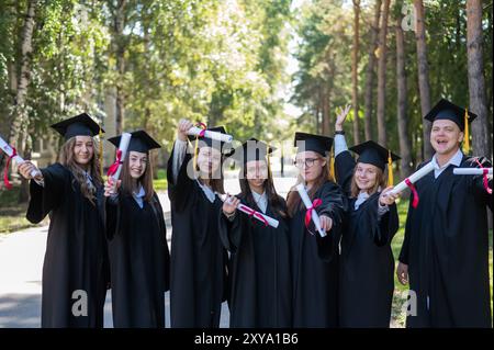 Rangée de jeunes étudiants dans les robes de diplôme en plein air montrant leurs diplômes. Banque D'Images