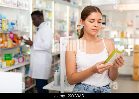 Adolescente choisissant des produits de soins capillaires en pharmacie Banque D'Images