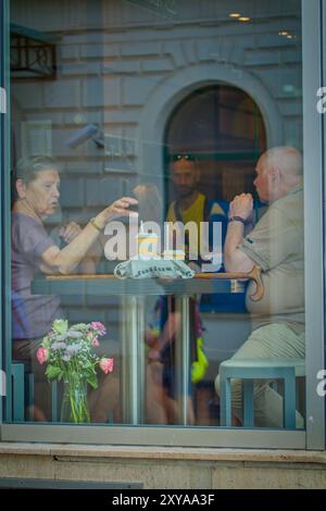 Couple senior assis dans McDonalds, photographié à travers la fenêtre reflétant la rue à l'extérieur Banque D'Images
