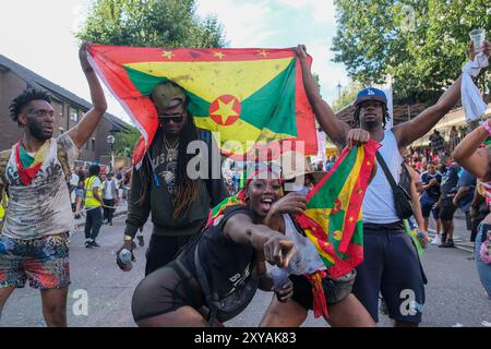 Londres, Royaume-Uni. Les fêtards brandissent le drapeau grenadan alors qu'ils passent devant la zone de jugement de la route du carnaval de Notting Hill le jour de l'adulte. Banque D'Images