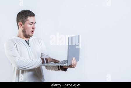 Gars surpris tenant et regardant une promotion sur l'écran d'ordinateur portable. Étonné bel homme debout à l'aide d'un ordinateur portable isolé Banque D'Images