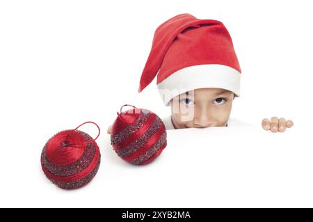 Garçon curieux dans le chapeau rouge avec deux boules décoratives de noël isolées sur fond blanc avec un espace de copie vide pour placer la publicité ou la bannière Banque D'Images