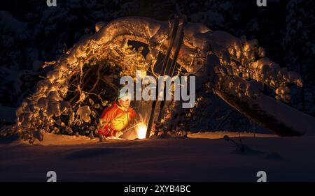 Homme griller des saucisses sur un feu de camp sous un pin enneigé, Gaellivare, Norrbotten, Laponie, Suède, novembre 2012, Europe Banque D'Images