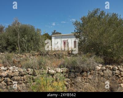 Maison peinte en blanc avec des portes rouges, entourée d'arbres et d'un jardin de rocaille sous un ciel clair, ibiza, mer méditerranée, espagne Banque D'Images