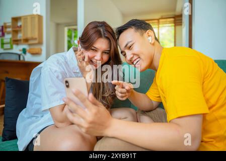 Les couples indonésiens sont assis sur un canapé, regardant un téléphone portable pendant un appel vidéo, écoutant de la musique ou regardant un film. L'homme pointe a Banque D'Images