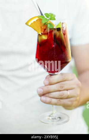 Verre de sangria glacé avec fraise, orange, pomme et citron dans la main de l'homme. Close up Banque D'Images