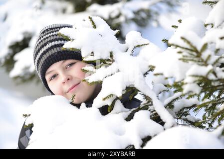 Teen Boy regarde derrière les arbres dans la forêt d'hiver Banque D'Images