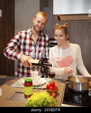 Couple heureux dans une cuisine la cuisson des pâtes et de boire le vin rouge Banque D'Images