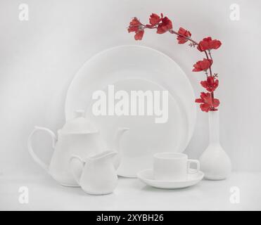 Nature morte affichant une théière blanche, une tasse, une soucoupe et des assiettes avec une fleur dans un vase. Gros plan, prise de vue en studio. Banque D'Images