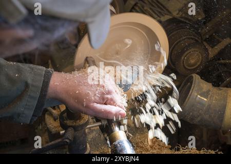 Fabrication d'un bol en bois sur un tour dans un ancien petit atelier avec des copeaux de bois volants Banque D'Images