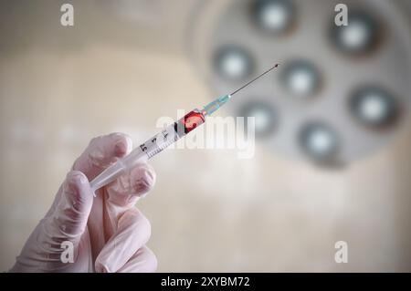 Gants en latex avec la main tenant une seringue d'un liquide rouge à l'intérieur, dans une salle d'opération Banque D'Images