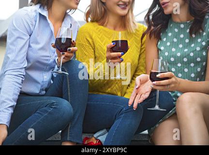 Trois jeunes femmes heureuses riant, buvant du vin rouge, s'amusant. Concept de fête et d'amitié. Mise au point sélective Banque D'Images