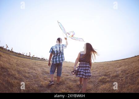 Petite fille et garçon heureux tournant avec un cerf-volant sur une prairie dans une soirée ensoleillée Banque D'Images