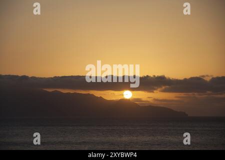 Mer avec le soleil couchant derrière quelques nuages Banque D'Images