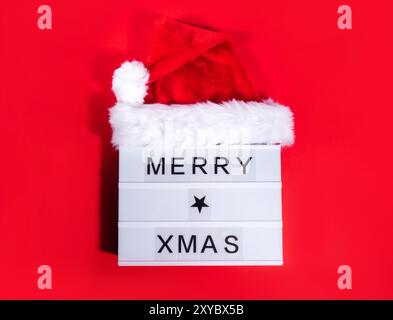 Joyeux Noël salutations de Noël sur lightbox avec chapeau de père noël sur fond rouge audacieux avec des ombres. Couche plate sombre des fêtes Banque D'Images