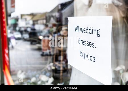 Un signe dans un magasin annonçant des robes de mariée à moitié prix dans une vitrine de magasin dans le centre de Newquay Town en Cornouailles au Royaume-Uni. Banque D'Images