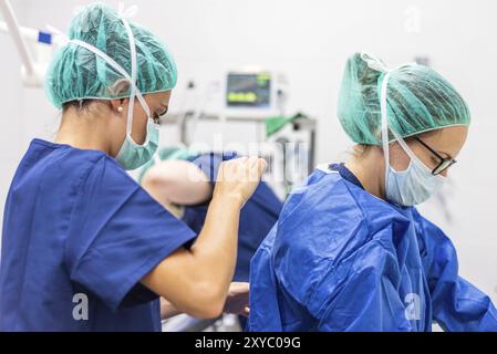 Assistant médical aidant un chirurgien à mettre des vêtements stériles une salle d'opération Banque D'Images