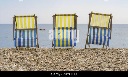 Empty Deck chaises sur la plage de galets à Beer, Devon, Royaume-Uni, regardant la baie de Seaton et la Manche britannique avec un petit bateau de pêche qui passe Banque D'Images