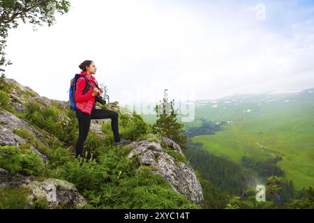 Hiker with backpack se détendre au sommet d'une montagne et profiter de la vallée durant le lever du soleil Banque D'Images