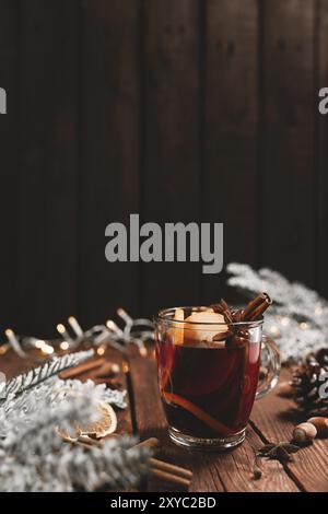 Photo concept de l'heure de Noël.Tasse ou mug en verre avec vin chaud à l'intérieur sur fond de table en bois.Décorations, cannelle, orange séché, pomme, divers Banque D'Images