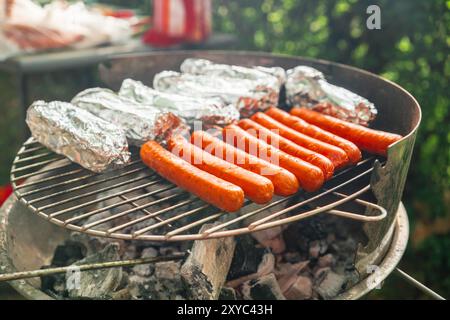 Saucisses rouges rôties sur un gril avec du fromage Feta enveloppé dans une feuille d'aluminium sur le gril au charbon Banque D'Images