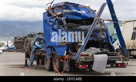 Gros plan sur une cabine de camion bleue bosselée et une semi-remorque sur une plate-forme de remorquage dans le stationnement après un accident grave. Banque D'Images