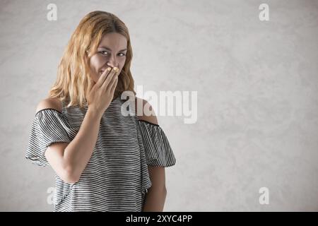 Fille timide couvrant son visage avec ses mains, dans un fond gris Banque D'Images