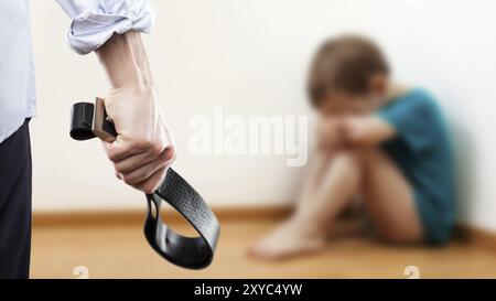 Concept de violence familiale et d'agression, furieux homme en colère levé la main de punition tenant la ceinture de cuir sur un garçon enfant effrayé ou terrifié assis à wa Banque D'Images