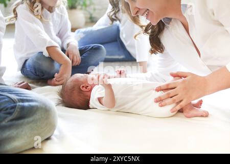 Grande famille avec trois enfants dans le salon blanc. Parents et enfants piquant par bébé nouveau-né. Mère, père et enfants jouant avec le chil nouveau-né Banque D'Images