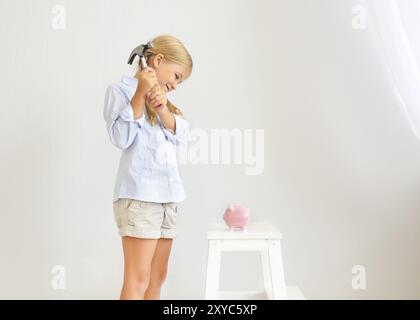 Petite fille avec un marteau par la tirelire cochon rose sur fond blanc Banque D'Images