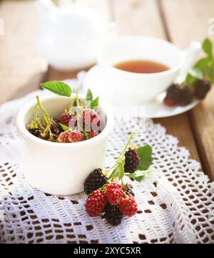 De dessus de framboise fraîche et de mûre avec des feuilles vertes sur table en bois avec un tissu tricoté blanc et une tasse de thé aromatique Banque D'Images