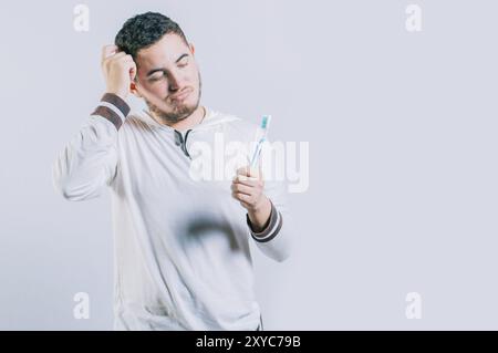 Jeune homme inquiet tenant la brosse à dents isolée. Gars réfléchi tenant et regardant la brosse à dents isolé Banque D'Images