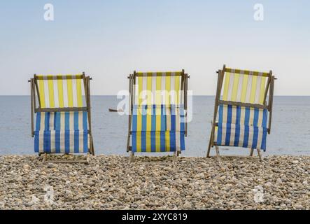 Empty Deck chaises sur la plage de galets à Beer, Devon, Royaume-Uni, regardant la baie de Seaton et la Manche britannique avec un petit bateau de pêche qui passe Banque D'Images