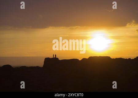 Deux personnes debout sur une crête de montagne lointaine silhouette par un grand soleil couchant juste au-dessus de l'horizon dans le désert de Gobi de Mongolie Banque D'Images