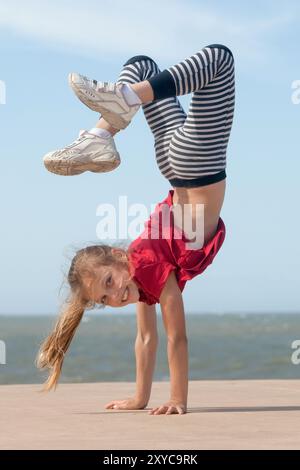 petite fille joyeuse faisant handstand près de l'océan le jour ensoleillé Banque D'Images