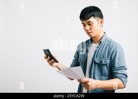 Un jeune homme, isolé sur blanc, semble triste, fatigué et tendu alors qu'il tient un papier et une calculatrice Banque D'Images