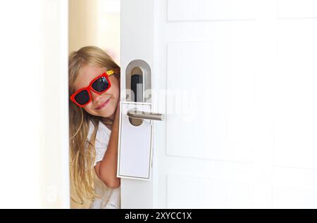 Happy little girl wearing sunglasses dans chambre d'hôtel ouvre la porte. Concept des vacances en famille Banque D'Images