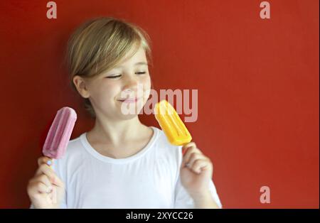 Petite blonde girl eating ice cream sur le fond rouge Banque D'Images