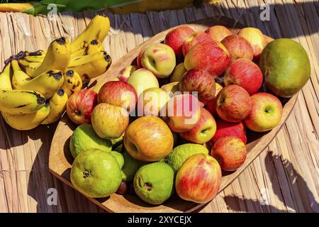 Bol en bois et matelas de paille rustique avec divers les goyaves, les pommes et les bananes sous les rayons du soleil Banque D'Images