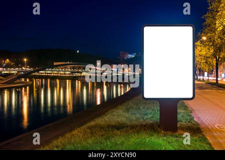 Maquette de panneau d'affichage vertical sur la rive de la rivière la nuit. Affichage publicitaire devant City Reflections Banque D'Images