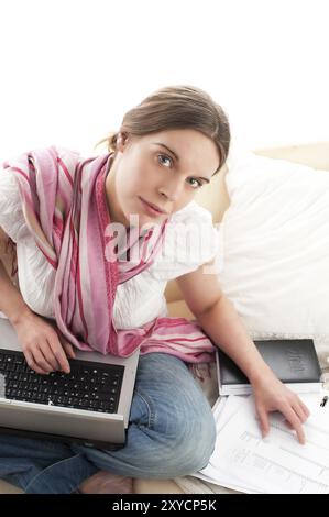 Jeune femme, assise sur un canapé et faisant un peu de travail de bureau avec un cahier et des documents. Texte espace libre, recadré jolie jeune femme, assise sur un cou Banque D'Images