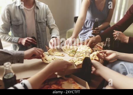 Une fête de pizza, un groupe d'amis discutant et se réjouissant de manger de la pizza à la table et de boire de l'eau douce de soda. Beaucoup d'amis se sont remis ensemble beca Banque D'Images