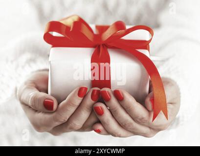 Woman's hands holding manucure rouge avec petite boîte-cadeau blanche avec ruban rouge Banque D'Images