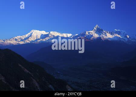 Les sommets enneigés reflétant l'aube soleil sur l'Annapurna de montagnes de l'Himalaya et d'une sombre vallée au Népal Banque D'Images